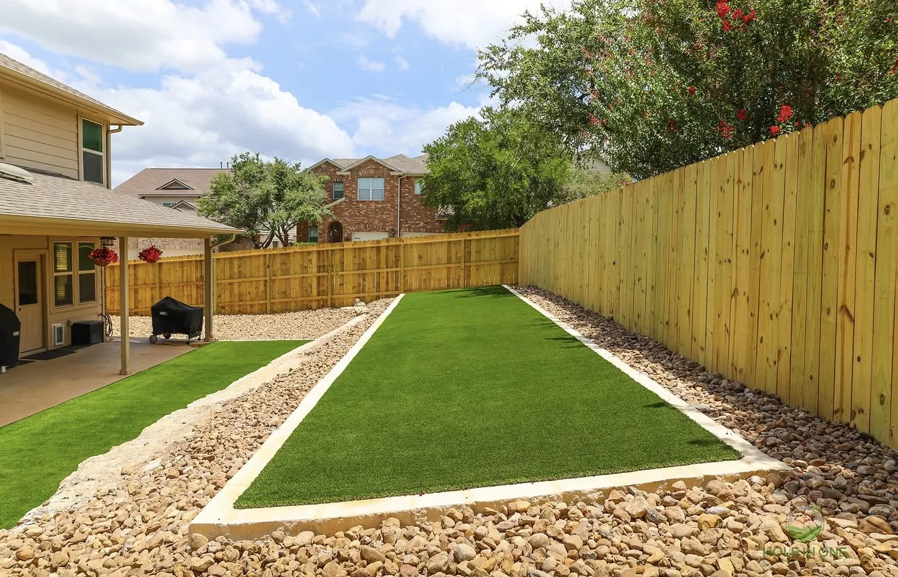 Artificial turf lawn edged with river rock and a paver border along a new cedar fence
