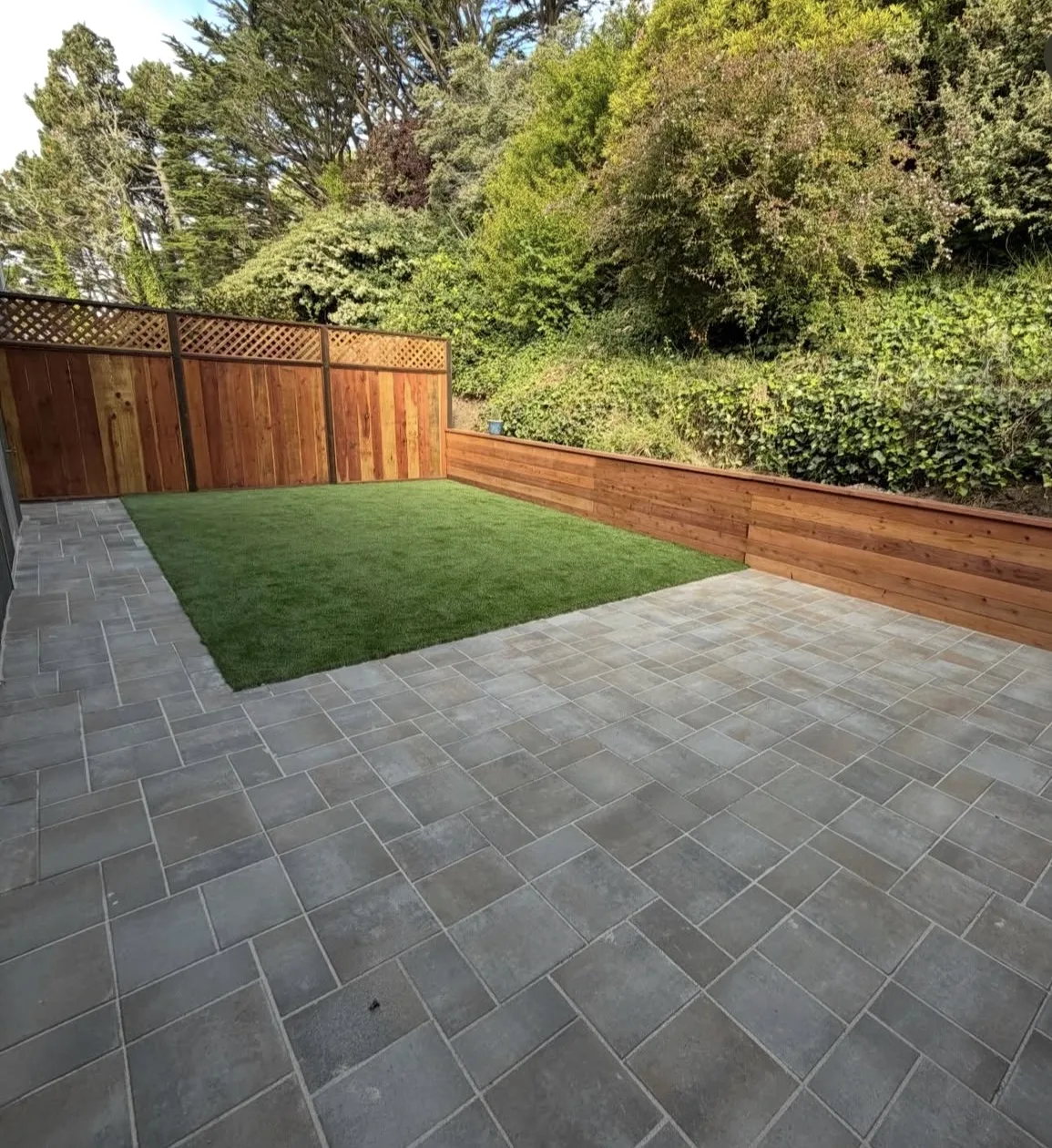 Artificial turf lawn beside a grey paver patio and a cedar retaining wall
